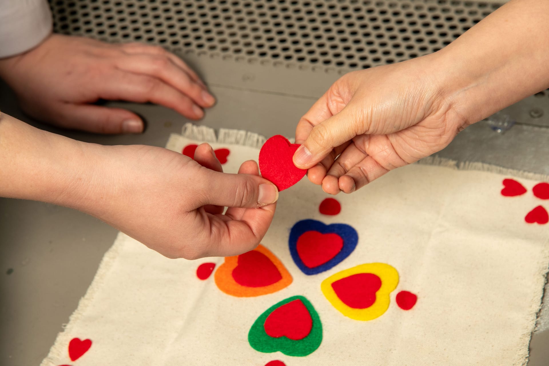 two people working together to make a piece of art by arranging colorful felt hearts on plain fabric